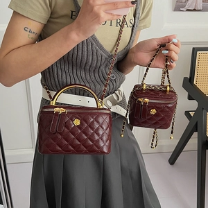 Detail view of burgundy quilted vanity cases with gold floral logo and chain straps