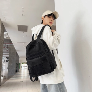 Detail of a minimalist black canvas backpack worn by a model in a modern urban corridor