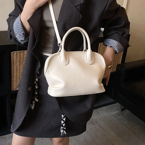 Close-up of beige shell handbag with cylindrical handle and detachable shoulder strap