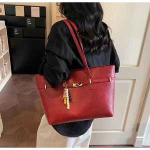 Detail of red leather tote bag with colorful beaded charm and metallic buckle closure
