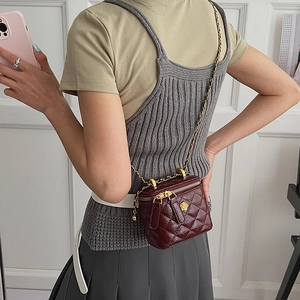 Detail of burgundy quilted leather crossbody bag with golden flower logo and chain strap