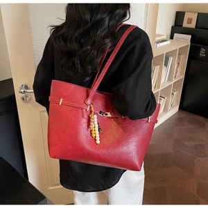 Detail view of red leather tote bag with vintage bead charm and metal buckle design