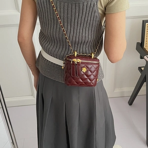 Detail of burgundy quilted box bag with gold flower accent and leather chain strap