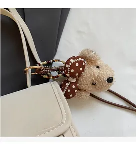 Detail of plush dog bag charm with red polka dot bow on a beige leather handbag