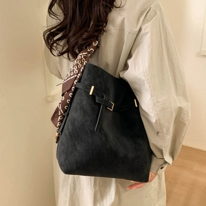 Close-up of black bucket bag featuring golden buckle strap and floral scarf detail