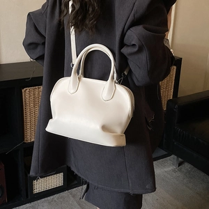 Detail view of cream white leather shell bag worn cross-body with adjustable slim strap