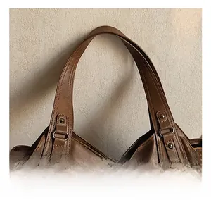 Detail showing the sturdy handle connection and stitching on the brown leather pillow bag
