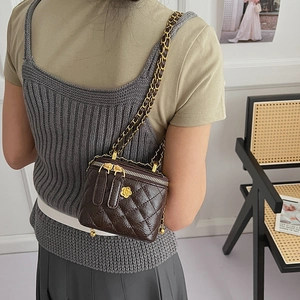 Detail of a dark brown quilted patent leather camera bag with gold camellia charm