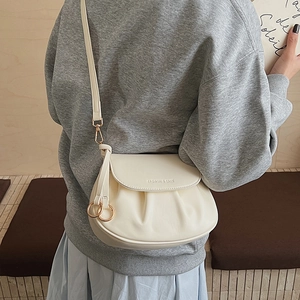 Close-up of pleated ivory crossbody bag with fashion text and gold ring hardware