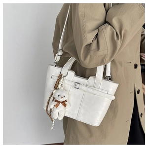 Weiße PU-Leder-Eimertasche mit Plüschbären-Anhänger getragen zu einem khakifarbenen Trenchcoat