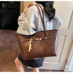 Detail of a brown leather tote bag with ethnic wooden bead charm on a model shoulder
