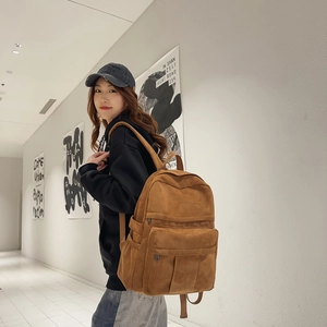 Detail of a brown suede backpack with a large front pocket shown in a modern art gallery