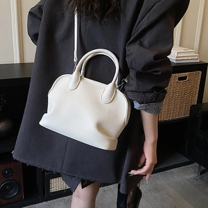Close-up of white lychee textured crossbody bag held by a model in a gray suit