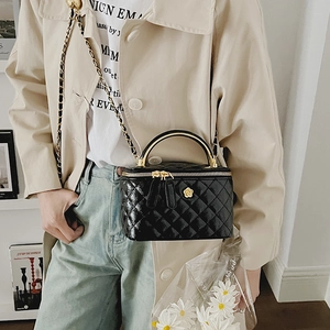 Close-up of black quilted box bag with gold floral clasp and woven chain strap