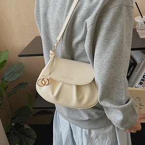 Detail view of beige pleated crossbody bag with gold hardware worn by model in a cafe