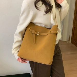 Detail of a large yellow leather bucket bag with golden buckle and protective base studs