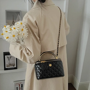 Detail of black quilted leather crossbody box bag with gold metal handle and chain strap