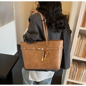 Detail view of tan leather tote bag featuring golden lock and colorful beaded charm