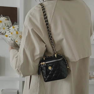 Elegant black quilted crossbody bag with gold camellia buckle on tan trench coat
