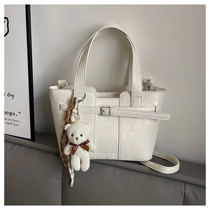 Detail der cremefarbenen Leder-Eimertasche mit Modeprägung und Plüschbär-Anhänger