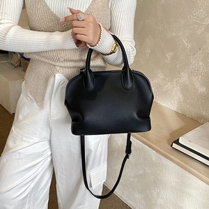 Detail of black lychee grain leather texture and adjustable strap on a shell-shaped bag