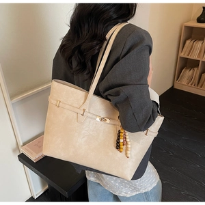 Detail of cream white tote bag with beaded charm on model wearing a grey blazer