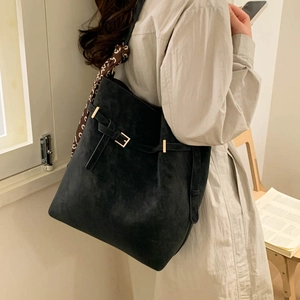 Black faux suede tote bag with decorative scarf and golden hardware in a home setting