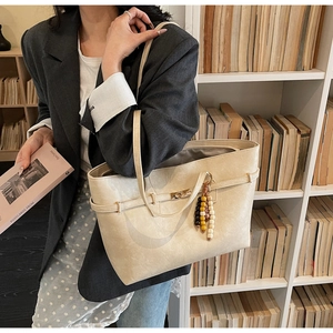 Detail view of beige faux leather tote with golden buckle and colorful bead tassel