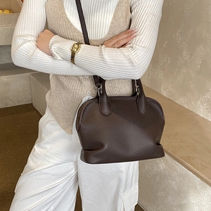 Brown lychee leather shell bag shown on model with shoulder strap and dual handles
