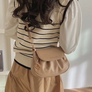 Detail of beige pleated crossbody bag with gold hardware worn by a model in casual outfit