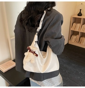 Detail of white PU leather hobo bag featuring a cute plush bear charm and knotted shoulder strap