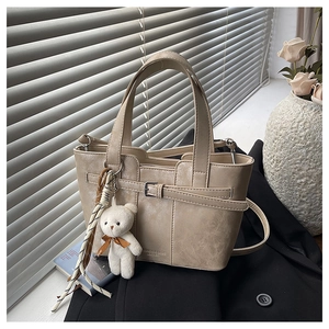 Detailansicht der beigen PU-Leder Eimertasche mit Zierschnalle und Plüschbär-Anhänger