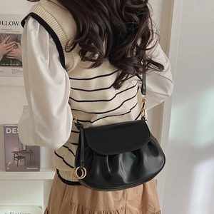Detail of black pleated saddle bag with gold metal rings and embossed fashion logo