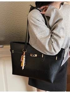 Classic black faux leather tote bag with vintage beaded charm on a casual grey sweatshirt