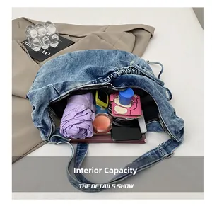 Makroaufnahme der großen Innenkapazität der blauen Denim-Schultertasche mit Alltagsdingen