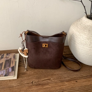 Close-up of deep brown suede bucket bag with gold clasp and horse charm