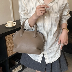 Detail of taupe lychee grain leather handbag featuring classic shell-shaped silhouette