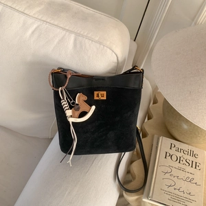 Detail of black leather bucket bag with suede texture and gold clasp featuring wooden horse charm