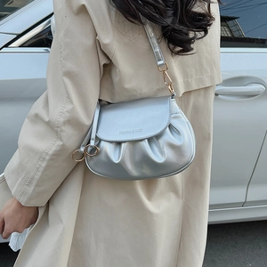 Close-up of a silver pleated half-moon bag with gold metal hooks on a beige trench coat