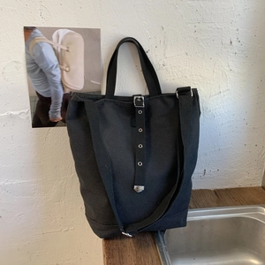 Détail d'un sac seau en toile noire avec œillets métalliques et bandoulière réglable