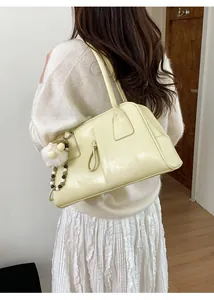 Detail of cream leather shoulder bag with plush ball charm shown on a model side view