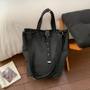 Détail d'un sac seau en toile noire avec œillets métalliques et lanière décorative en cuir
