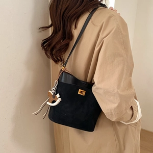 Detail view of black bucket bag with gold clasp and rocking horse charm on beige coat