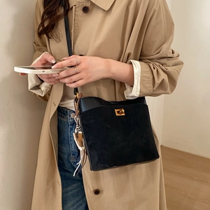 Detail of black leather bucket bag with gold clasp and tassel worn on khaki trench coat