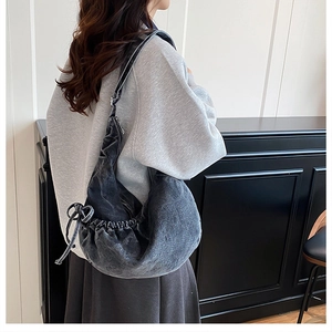 Detail der grauen Denim-Hobo-Tasche mit seitlicher Schleife und schwarzem Lederriemen