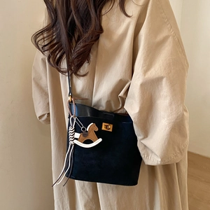 Detail of black crossbody bucket bag with gold clasp and wooden horse charm decoration