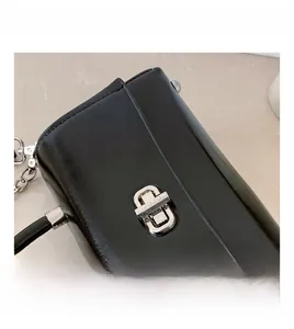 Close-up of a silver rectangular metal twist lock on a glossy black leather shoulder bag