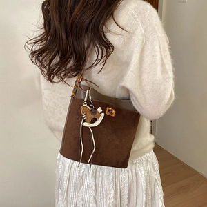 Brown suede bucket bag with gold lock and horse charm worn over the shoulder