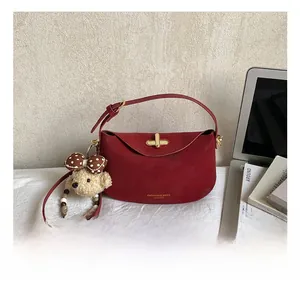 Close-up of a vintage red leather shoulder bag featuring a gold clasp and plush bear charm