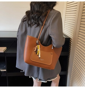 Dettaglio della borsa tote in pelle marrone con ciondolo a nappa in legno sul manico